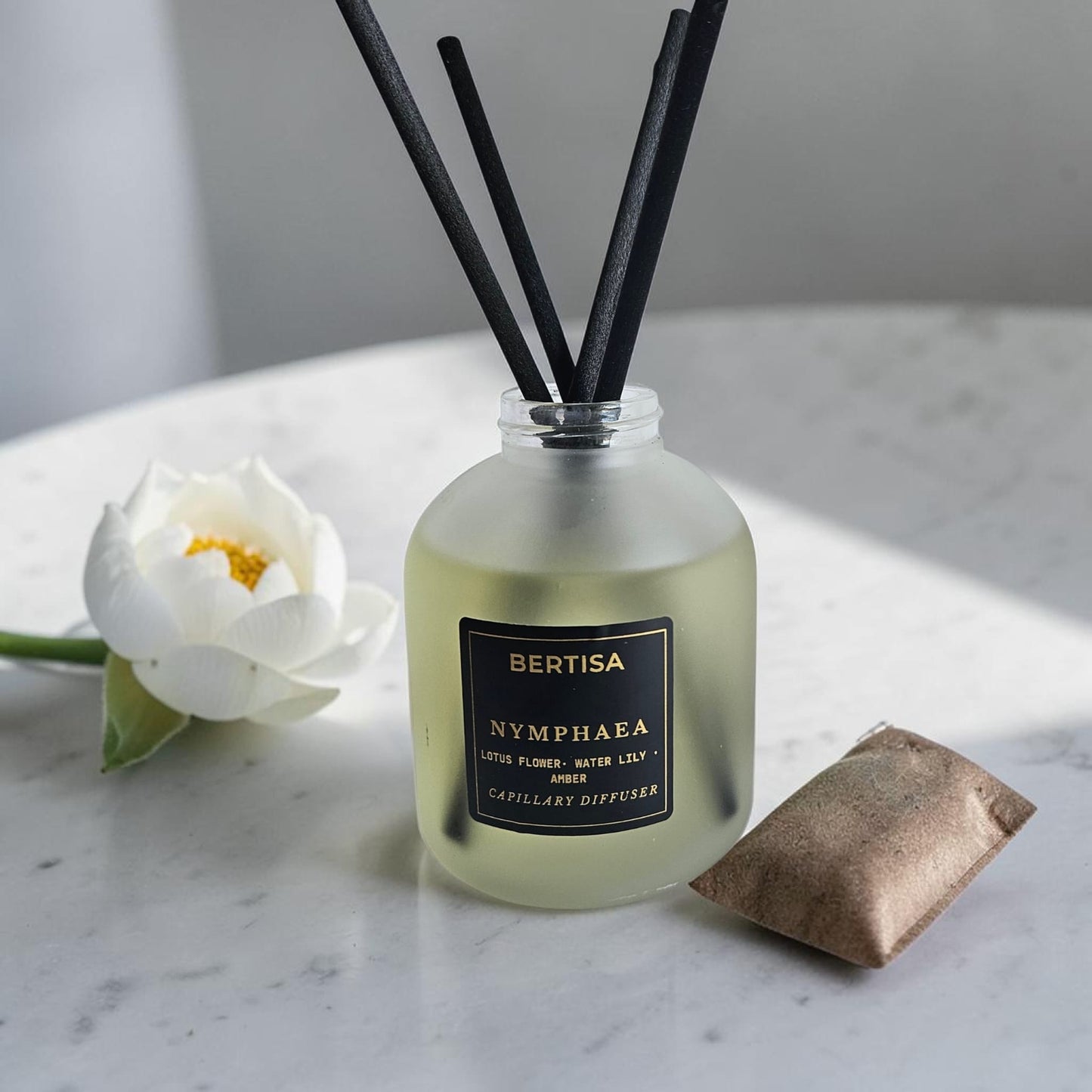 Bertisa Nymphaea diffuser with black reeds and a white flower on a marble surface.