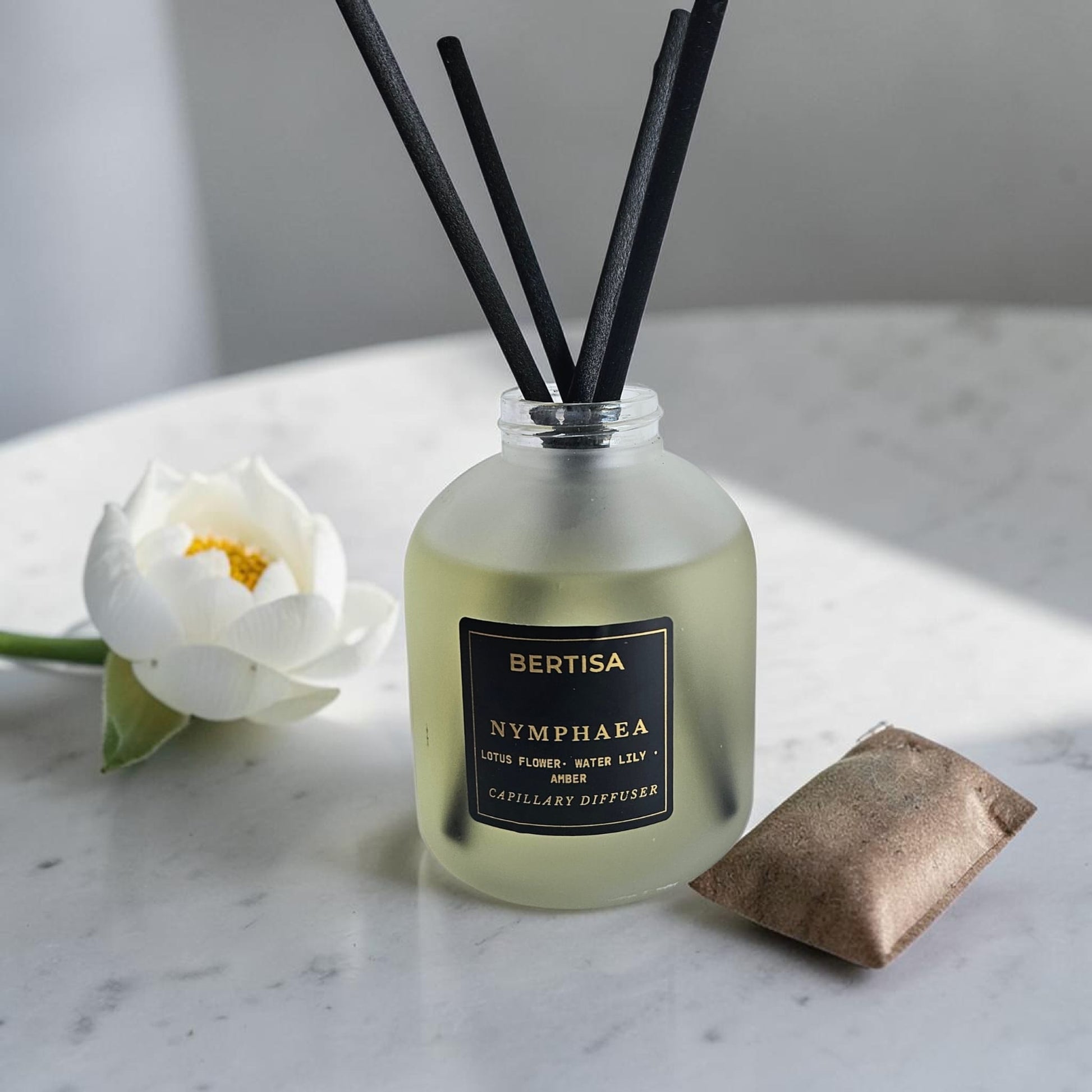 Bertisa Nymphaea diffuser with black reeds and a white flower on a marble surface.