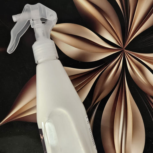 White spray bottle with a clear nozzle against a decorative brown and black background