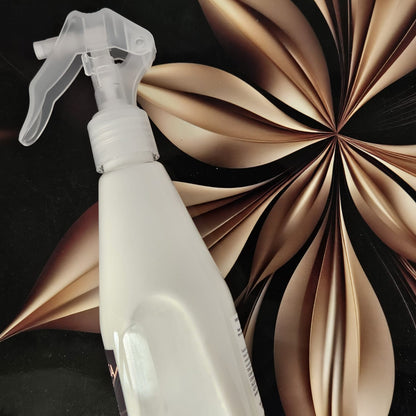 White spray bottle with a clear nozzle against a decorative brown and black background